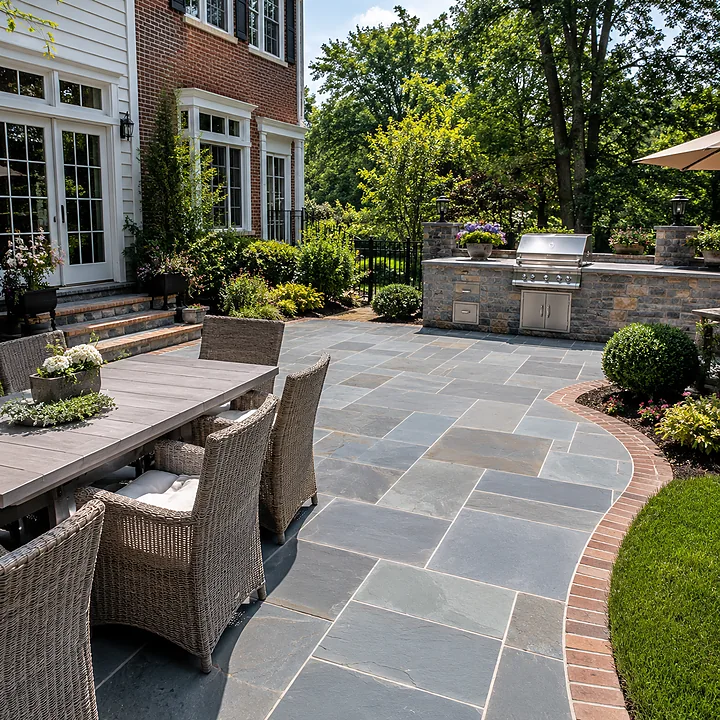AM Developers LLC built a natural bluestone and flagstone patio in Gaithersburg, MD, with thermal-cut stone paving, brick borders, dining furniture, grill station, and landscaped garden beds.